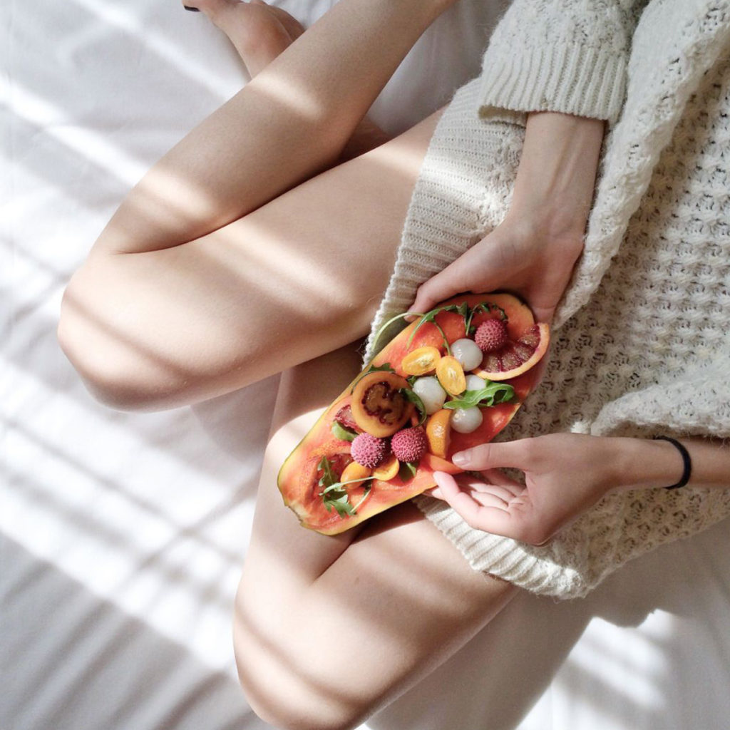 chica en la cama comiendo papaya con frutas